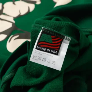 Label on green hoodie featuring "Made in USA" tag with American flag design, showcasing high-quality fabric from Denim Tears Cotton Flower brand.