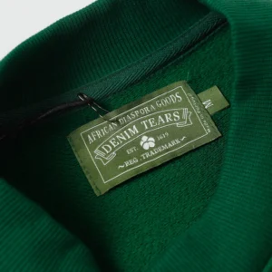 Label of Denim Tears Cotton Flower hoodie, featuring brand name and logo on green fabric.