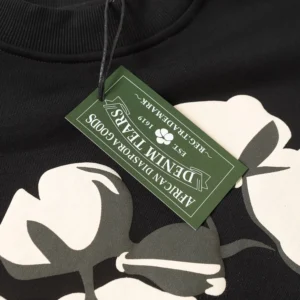 DENIM TEARS Cotton Flower hoodie featuring a black fabric background, large floral print, and a green tag displaying the brand name and details.