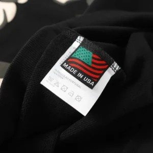 Label tag on a black hoodie featuring "MADE IN USA" text and American flag design, showcasing the quality and origin of the DENIM TEARS Cotton Flower hoodie.