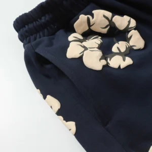 Denim Tears Cotton Flowers printed shorts in navy blue with beige floral foam flocking design, showcasing trendy streetwear style.