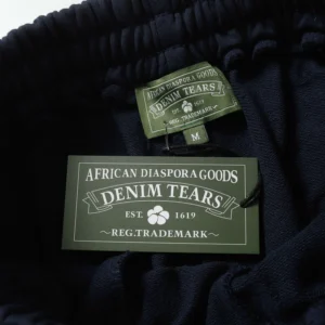 Denim Tears label on cotton shorts featuring "African Diaspora Goods" and trademark details, highlighting the trendy streetwear brand's identity.