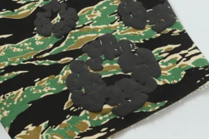 Cotton fabric featuring camouflage pattern with black foam flocking floral designs, representing DENIM TEARS Cotton Flower shorts.