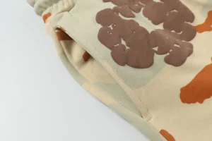 No brand or clear product type visible; a close-up of beige fabric with brown embossed text and orange accents.
