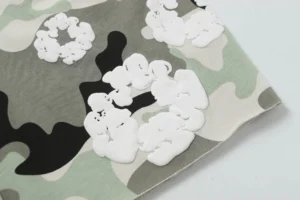 Cotton fabric featuring camouflage pattern with white floral appliqués, representing Denim Tears Cotton Flower design.