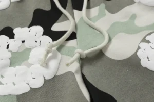 Close-up of Denim Tears Cotton Flower shorts featuring camouflage pattern and white foam flocking details, showcasing drawstring ties.