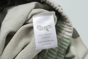 Label of Denim Tears Cotton Flower shorts showcasing care instructions and material details, featuring camouflage design elements.