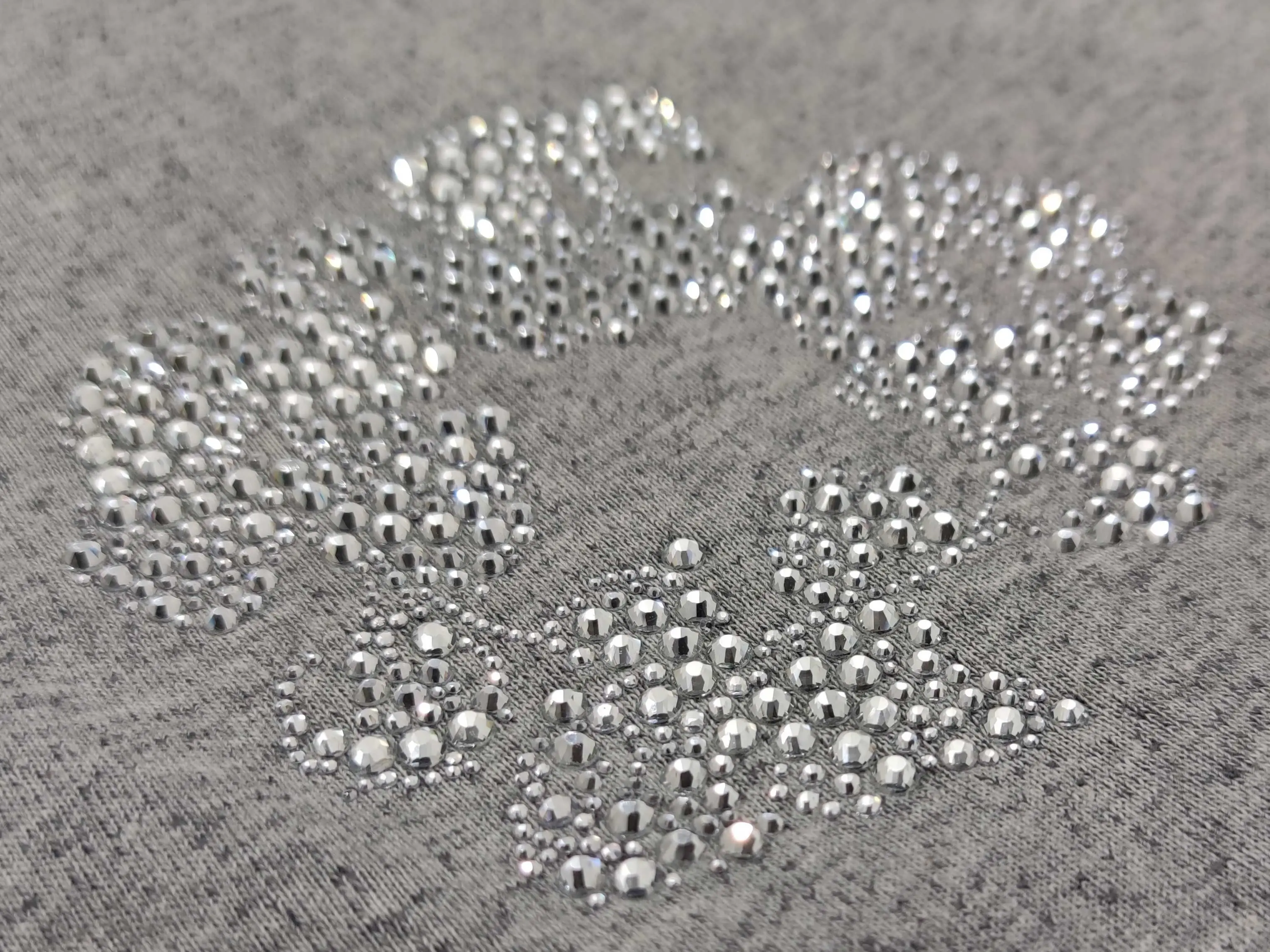 No brand or product type visible, close-up of silver rhinestones on grey fabric forming a patterned design accessory