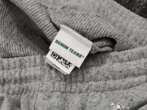 Denim Tears clothing tag green text woven label on grey knit fabric material