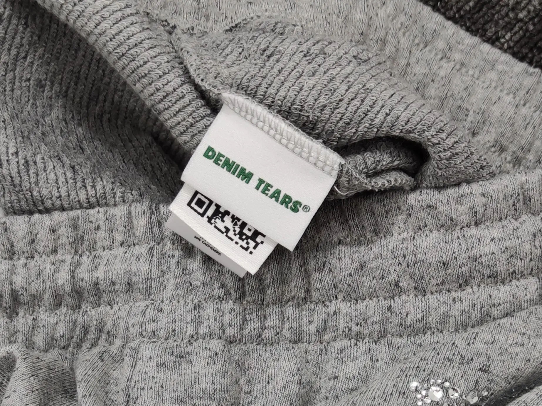 Denim Tears clothing tag green text woven label on grey knit fabric material