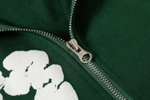 Close-up of a green hooded sweatshirt featuring a zipper and a white floral design, part of the DENIM TEARS Cotton Flower collection.