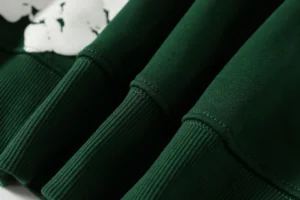 Close-up of DENIM TEARS Cotton Flower hooded sweatshirt in green, showcasing ribbed cuffs and soft fabric texture, highlighting quality and style.