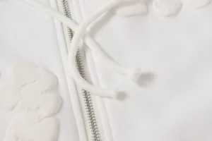 Unable to generate alt text based on the provided product type rules as the image shows a close-up of a white fabric garment with a zipper and drawstrings, not watches, sneakers, bags, or accessories. Please provide product type details.