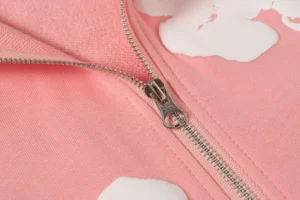 Close-up of a pink hoodie zipper featuring white cloud designs, highlighting the high-quality fabric and stylish details of the DENIM TEARS Cotton Flower hoodie.