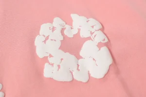 Close-up of a pink fabric featuring a white floral design, representing the DENIM TEARS Cotton Flower hoodie, emphasizing its stylish and eco-friendly aesthetic.