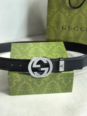 Gucci men's leather belt featuring a double G logo buckle, displayed on a green patterned box with a Gucci shopping bag in the background.