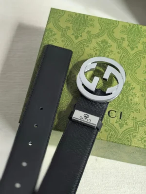 Gucci men's leather belt featuring a double G logo buckle and a metal tag with "GUCCI" inscription, displayed on a green patterned box.