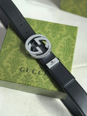 Gucci men's leather belt featuring a double G logo buckle and embossed metal tag, displayed on a green Gucci box, emphasizing luxury craftsmanship and brand recognition.