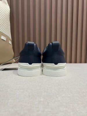 Navy leather slip-on shoes for men with a minimalist design, featuring a white rubber sole, placed on a textured surface, highlighting premium craftsmanship and style.