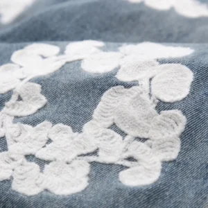 Close-up of DENIM TEARS Water Washed Embroidery Vintage jeans featuring intricate white floral embroidery on denim fabric.