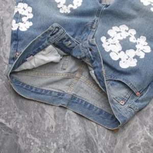 Vintage denim jeans with water washed finish and white floral embroidery, showcasing the waistband and inner lining, presented in a stylish flat lay on a textured surface.