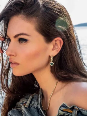 Model showcasing Apm Monaco Peacock Stone Love Circle Earrings, featuring a heart-shaped design, set against a natural outdoor backdrop.