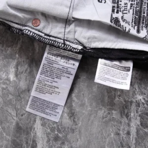 Levi's jeans care tags with manufacturing and washing instructions in multiple languages on gray fabric background