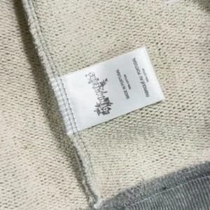 Label tag of Denim Tears hoodie featuring brand logo and care instructions on a textured fabric background.