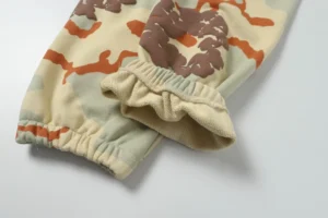 High-quality camo printed looped sweatpants from Denim Tears, featuring elastic cuffs and a blend of beige, brown, and orange colors.