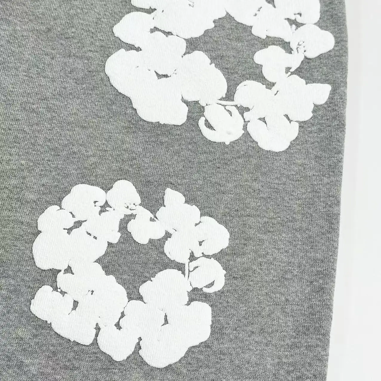 White floral design on grey fabric, representing Denim Tears Main Line Hemp Grey Cotton pants, emphasizing cotton texture and unique print details.