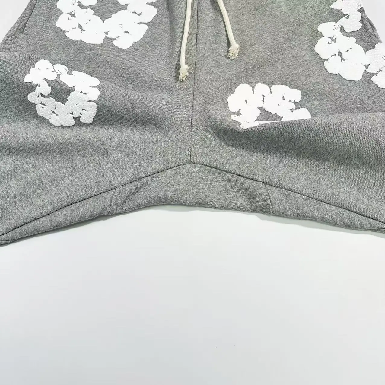 Grey cotton pants from Denim Tears featuring white floral prints and drawstring waist, showcasing fabric texture and design details.