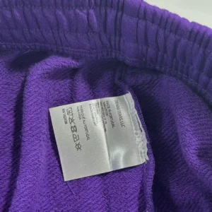 Label inside purple sweatpants from Denim Tears, showcasing fabric texture and care instructions.