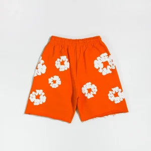 Denim Tears mainline orange shorts featuring white kapok flower designs, showcasing vibrant color and unique pattern.