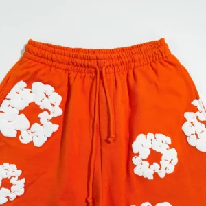 Denim Tears mainline orange shorts featuring white kapok flower designs, showcasing the fabric texture and elastic waistband.