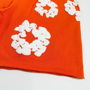 Denim Tears mainline orange shorts featuring white kapok flower embroidery on a vibrant orange fabric.