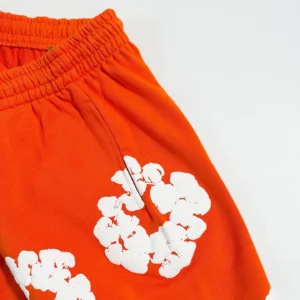 Orange shorts featuring white kapok flower design, part of Denim Tears mainline collection, suitable for casual wear and available for purchase.