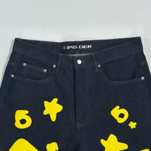 Sp5der Beluga Star Original Color Jeans featuring a dark denim fabric and bold yellow star and circle graphics, showcasing the brand logo on the waistband.