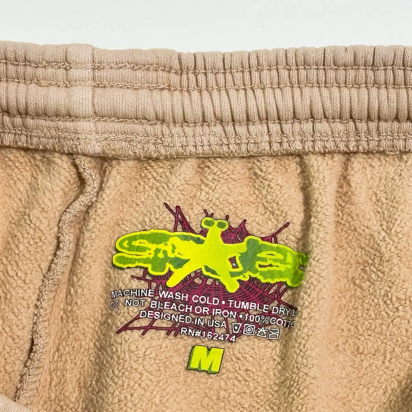 Sder Camel Beluga Sweatpants 05 featuring vibrant logo design, care instructions, and size label, emphasizing premium fabric quality and unique style.