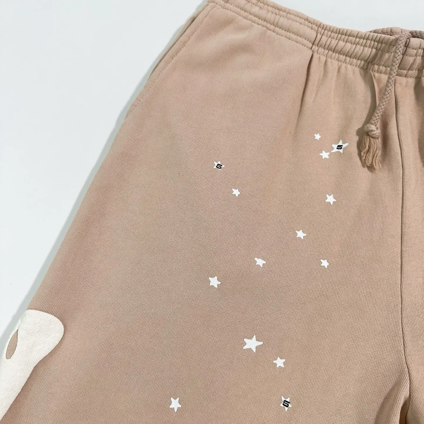 Sder Camel Beluga Sweatpants 05 in beige with white star prints and logo detail, showcasing fabric texture and design elements.