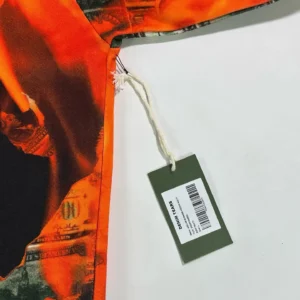 Denim Tears Burning Dollar Hoodie fabric detail showcasing vibrant orange design and product tag.