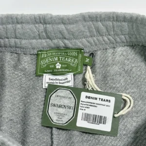 Denim Tears grey sweatpants interior label featuring Swarovski crystals, brand tag, and care instructions.