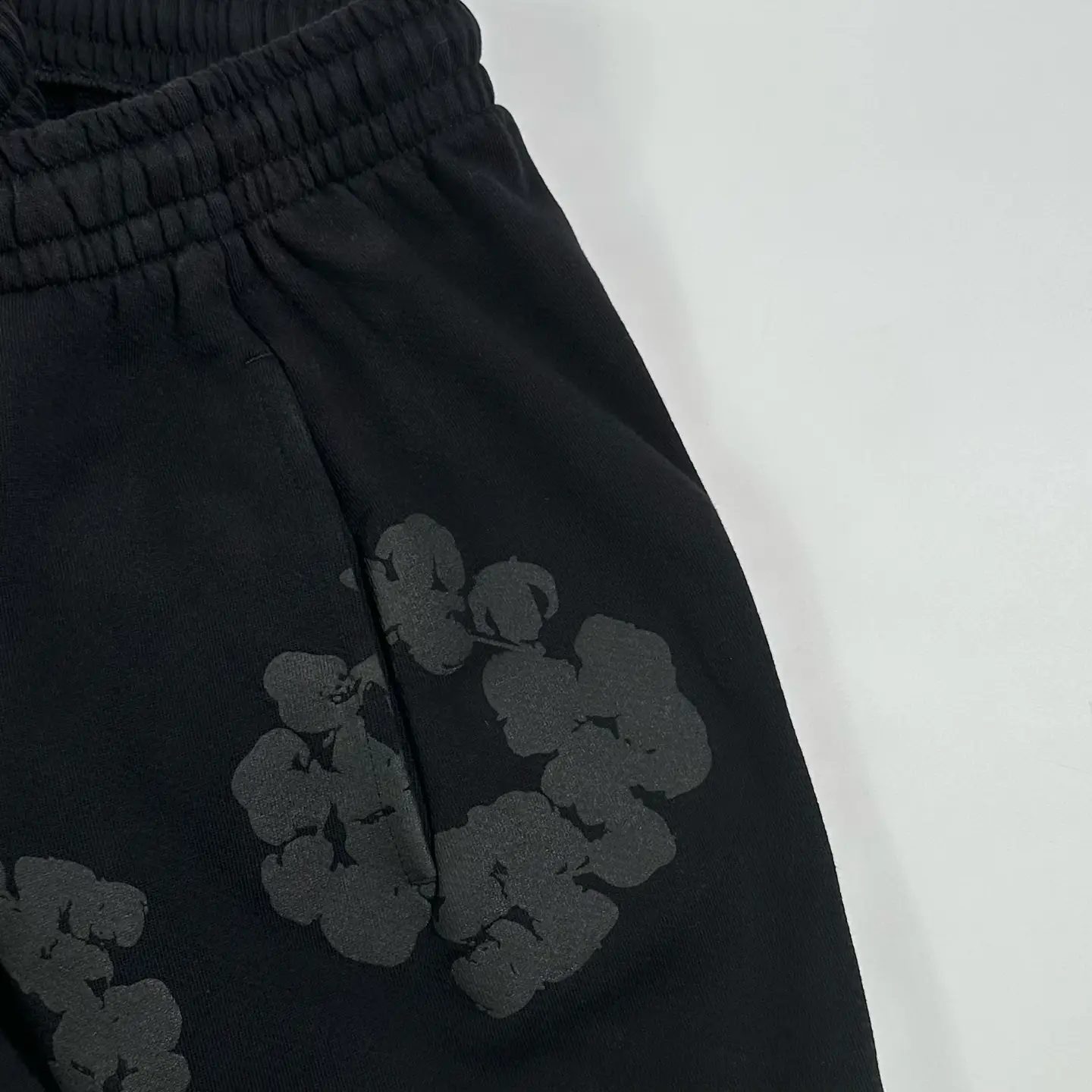 No brand or product type visible; image shows black fabric with subtle dark floral print and elastic waistband.