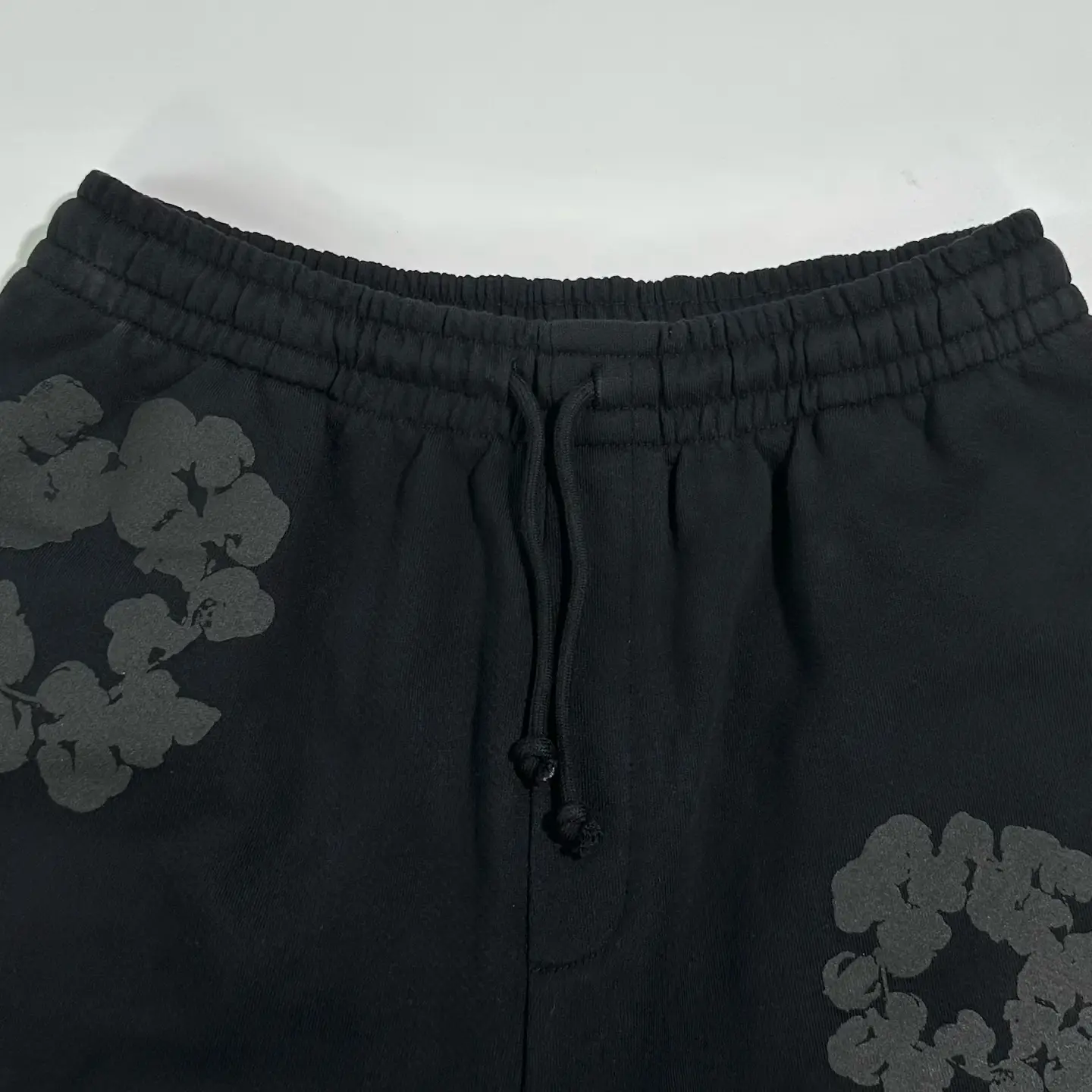 Represent black sweatpants with elastic waistband and drawstring closure made of cotton material with floral print detail