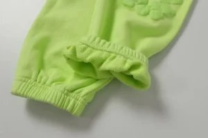 Close-up of Denim Tears cotton flower pants in fluorescent green, showcasing elastic cuff detail and textured floral design.