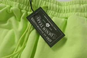 Denim Tears cotton flower shorts in fluorescent green with tag displaying brand name and care instructions.