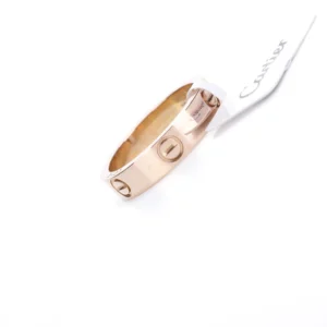 Cartier LOVE Series Ring in rose gold, featuring iconic screw motifs and a tag with the brand name.