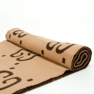 Gucci GG Large Logo Jacquard Wool Scarf rolled up, showcasing the signature GG logo in brown on a beige background, highlighting luxury fashion accessory details.