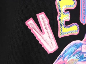 Versace Painted Sequins Medusa People sweatshirt detail featuring colorful sequins and bold lettering on black fabric.