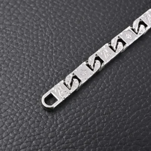 Louis Vuitton Monogram Tied bracelet featuring polished metal with interconnected nameplates and LV letters on a textured black background.