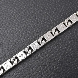 Louis Vuitton Monogram Tied bracelet featuring polished metal with intricate LV letters and Monogram flower carvings, displayed on textured black surface.